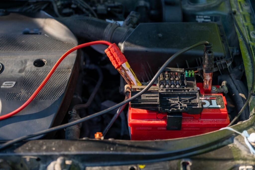 Close-up of a car battery with attached jumper cables in an engine bay.