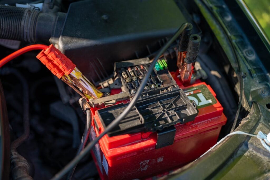 Close-up view of a car battery with red jumper cables connected, outdoors.